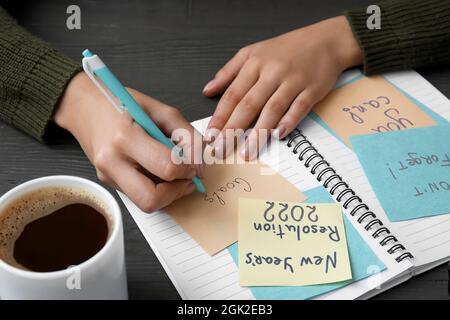 Woman writing word GOALS on sticky note at black wooden table, closeup Stock Photo