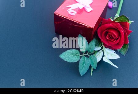 A red rose and a wrapped gift box with ribbon on table in blue background. High angle view. Flat Lay. Copy space room for text. Stock Photo