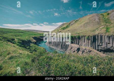Overview of Studlagil canyon in Iceland, picturesque valley with basalt columns standing high on a warm summer day. Shot taken trough grass Stock Photo