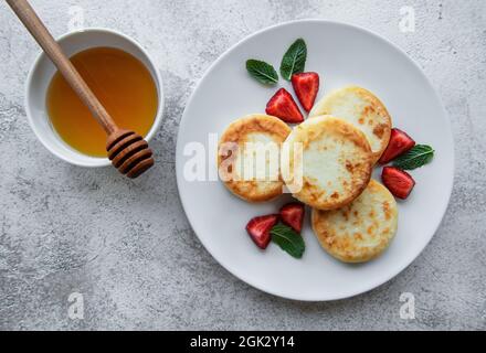 Cottage cheese pancakes, ricotta fritters on ceramic plate with  fresh strawberry. Healthy and delicious morning breakfast.  Grey concrete background. Stock Photo