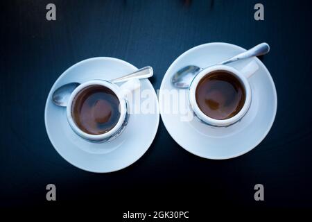 Two cups of coffee with round white plates and tea spoons on black table. View from above. Morning coffee in bar for a couple. Coffee espresso Stock Photo