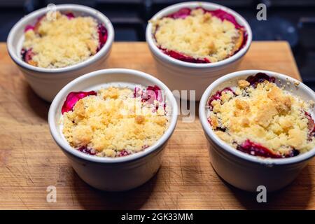 plums under the crumble in small white bowls placed on a wooden chopping board Stock Photo