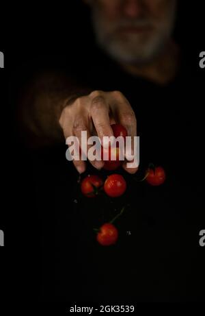 Hand dropping cherry tomatoes against black background Stock Photo