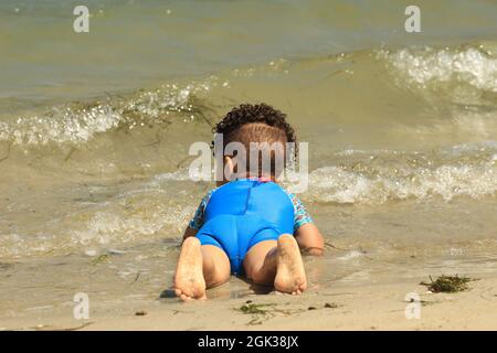 Cute little African child with curly hair laying on a beach