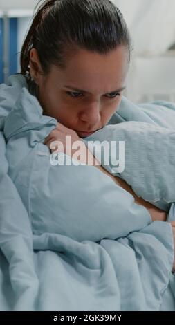 Ill woman with flu using blanket and pillow against shivering at home. Sick adult feeling cold and having chills because of fever symptoms. Close up of person with disease sitting on couch Stock Photo