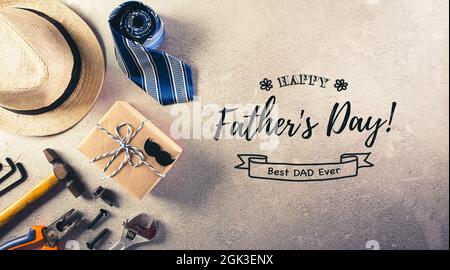 Happy Father's Day decoration with beautiful tie with mustache, hand tools, glasses, gift box and hat with the text on dark stone background. Stock Photo
