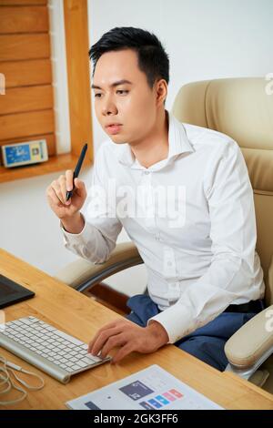 Pensive young UX designer working on computer at his office desk and creating new design Stock Photo