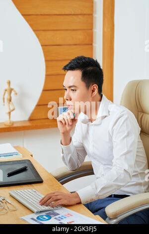 Pensive young graphic designer reading e-mail from customer containing requirement specification Stock Photo