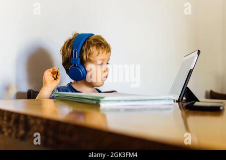 three-year-old boy attending an online class at school connected with the tablet at home watching the media Stock Photo