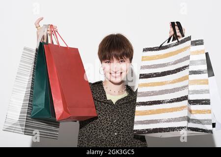 Portrait of young happy woman holding paper shopping bags in her hands and smiling at camera against the white background Stock Photo