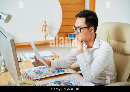 Pensive young UX designer reading document with requirement specification for new project Stock Photo