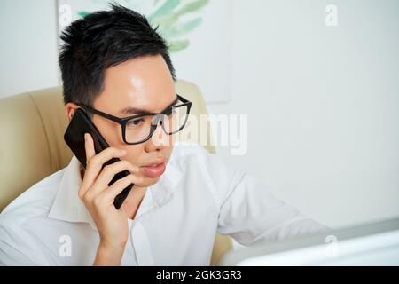 Serious young graphic designer making phone call to specify details of project Stock Photo