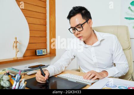 Concentrated young designer using digital pen and graphic tablet when drawing logotype for customer Stock Photo