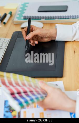 Graphic designer holding palette of color samples when drawing picture on graphic tablet with digital pen Stock Photo