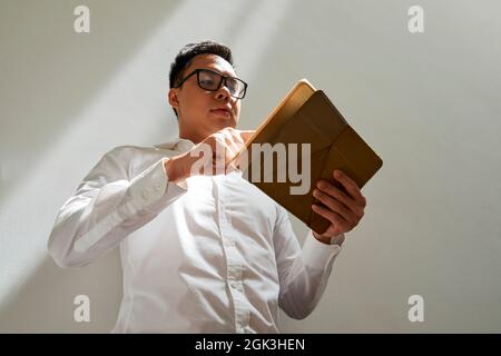 Businessman in white shirt and glasses checking document or e-mail on tablet computer, view from below Stock Photo
