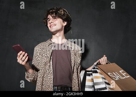 Young man with shopping bags using mobile phone for online shopping isolated on black background Stock Photo