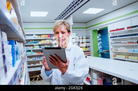 Caucasian senior pharmacist checking digital tablet walking through isles in pharmacy drugstore Stock Photo