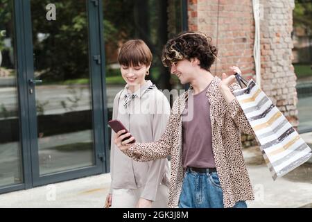 Young man showing new collection on the mobile phone to his girlfriend while they shopping together outdoors Stock Photo
