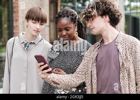 Group of friends using mobile phone together while walking in the city Stock Photo