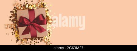 Banner with gift box with red ribbon and gold confetti on a beige background. Stock Photo