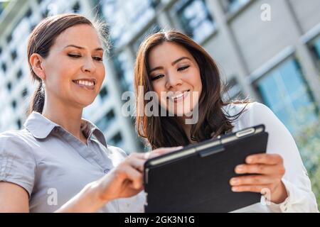 Business team of two successful women, mixed race group of businesswomen, Asian and Caucasian using a tablet computer in a modern city Stock Photo