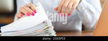 In front of businesswoman lies large pile of papers and stands laptop on desktop Stock Photo