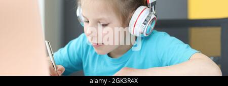 Girl in headphones makes notes in notebook on table is laptop Stock Photo