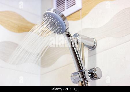 New shiny metal shower head with flowing water on ceramic tile wall background in the bathroom. Stock Photo