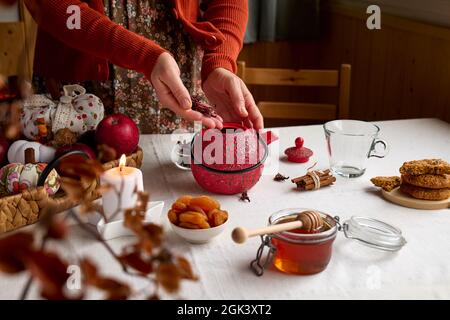 Cozy autumn days. Woman wearing orange sweater brew tea in red teapot on the table with linen tablecloth. Aromatic mood. Fall vibes. Tea drinking.Than Stock Photo