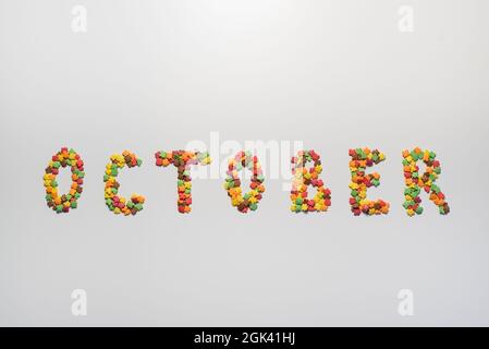 October inscription on a white background. Confectionery sprinkles in the form of multi-colored maple leaves Stock Photo