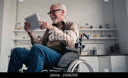 Smiling disabled pensioner in wheelchair using digital tablet at home Stock Photo