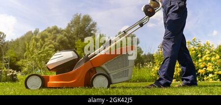 A professional gardener with a lawnmower cares for the grass in the backyard. Stock Photo