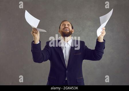 Young man holding sheets of paper and crying stressed with office job and business paperwork Stock Photo