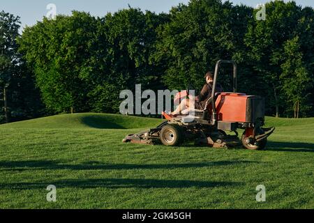 Greenkeeper. Golf course maintenance worker, cutting green grass Stock Photo