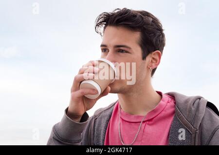 portrait of a handsome young student drinking a cup of coffee outdoors, concept of urban lifestyle, copy space for text Stock Photo