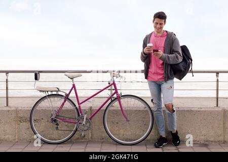 happy young student with a coffee smiling using smart phone near of his retro bicycle, concept of technology and sustainable urban transportation, cop Stock Photo