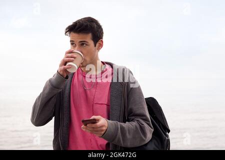 young man drinking coffee and using a mobile phone outdoors, concept of technology and communication, copy space for text Stock Photo