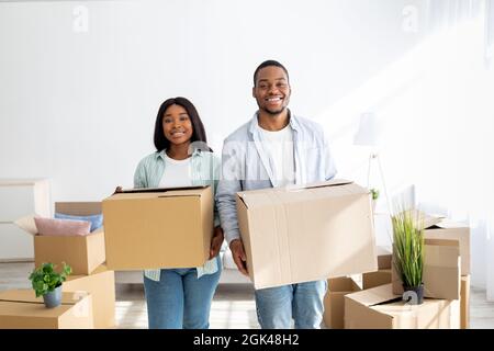 Relocation concept. Happy african american couple carrying cardboard boxes into new house, smiling at camera Stock Photo