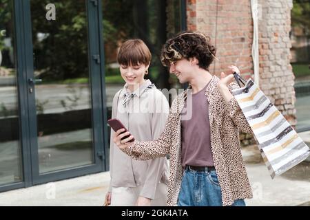 Young man showing new collection on the mobile phone to his girlfriend while they shopping together outdoors Stock Photo