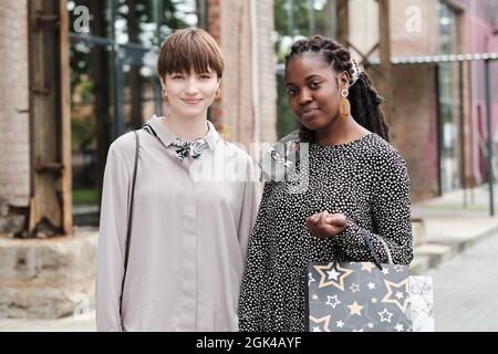 Portrait of two young friends with purchases looking at camera while having meeting in the city Stock Photo