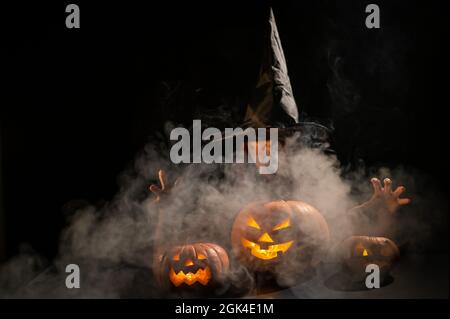 The evil witch casts a spell on pumpkins. Portrait of a woman in a carnival halloween costume in the dark Stock Photo