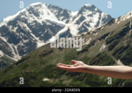 An empty open female palm against the background of beautiful mountains and blue sky. Closeup woman's hand showing something in empty copy space for a Stock Photo