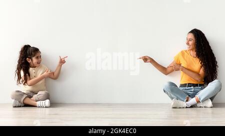 Happy Arab Mom And Daughter Pointing At Copy Space In The Middle Stock Photo