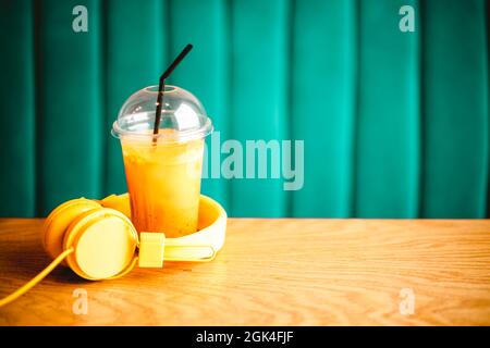 Fresh orange citrus juice, smoothie, or drink with straw and yellow headphones on cafe table. Basil blue or harbor green background, space for text Stock Photo