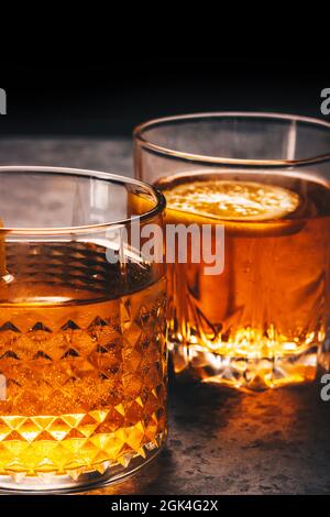 Alcohol drink in two rock glasses. Scotch whiskey, rum, bourbon, liquor, or brandy cocktails on the menu. Vertical dark design with space for text Stock Photo