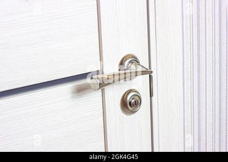 Closed white wooden door with modern metal doorknob in the house. Stock Photo