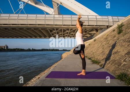 Young woman is exercising outdoor. She is practicing yoga on sunny day. Vriksasana, Tree pose. Stock Photo