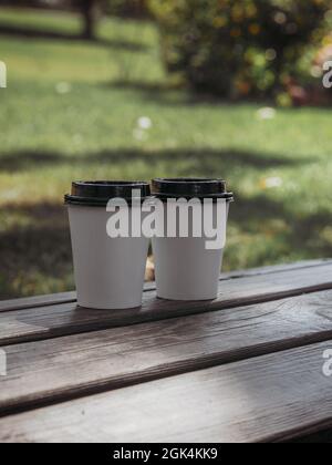 Two white paper cups of coffee on the background of a green park. Stock Photo