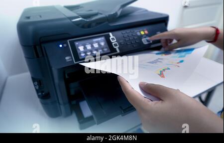 Office worker prints paper on multifunction laser printer. Copy, print, scan, and fax machine in office. Document and paper work. Print technology. Stock Photo