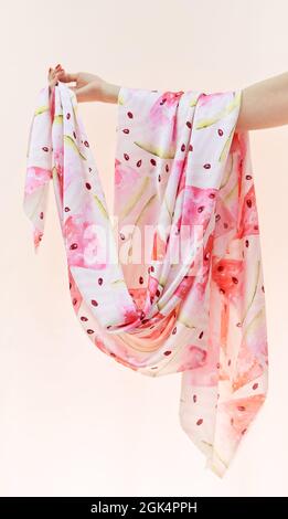 Closeup pastel colored silk or satin cloth fabrics in pink, brown and white colors hanging on woman's hand on beige background. Tailoring, seamstress or atelier concept. High quality vertical photo Stock Photo